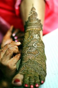 Cropped hand of mehendi artist applying henna tattoo on brides foot