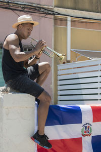 Full length of man playing trumpet while sitting on wall