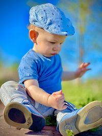 Portrait of a boy taken from below sitting against a blue sky wearing a blue beret and t-shirt blu