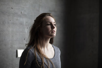 Beautiful young woman looking away while standing against wall