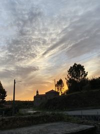 Silhouette trees by building against sky during sunset