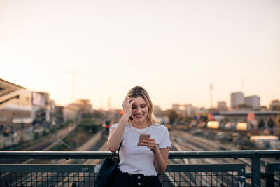 Portrait of smiling woman standing against railing in city