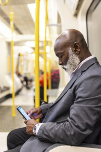 Bald senior businessman using mobile phone in subway train