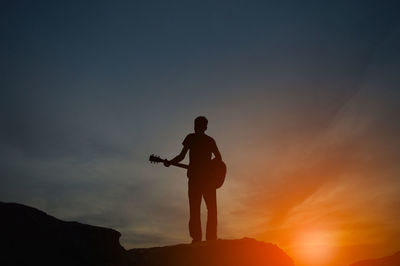 The shadow of a man holding a guitar on a hill with orange light