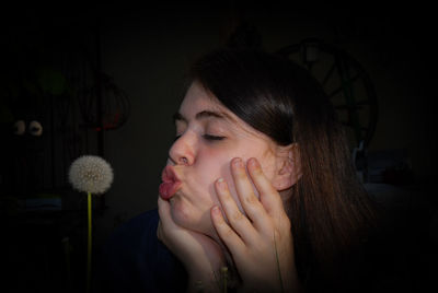 Close-up of young woman looking at dandelion flower at home