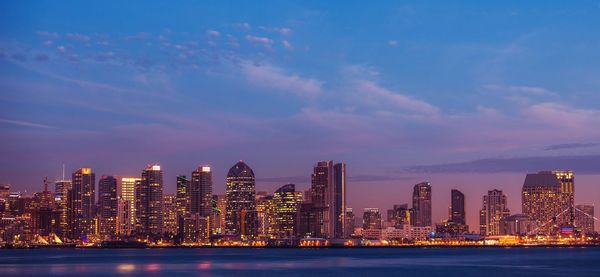 Illuminated city by buildings against sky