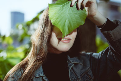 Close-up of smiling young woman covering face with leaf