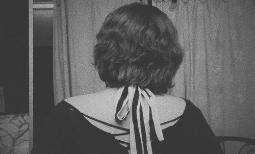 Rear view of woman standing against wall at home