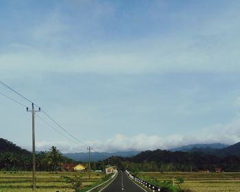 Road amidst field against sky