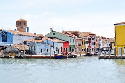 Boats in river by buildings in city against sky