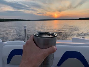 Cropped image of hand holding drink against sky during sunset