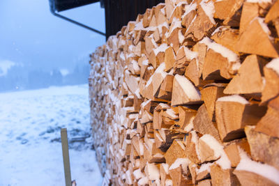 Freshly beaten firewood stacked against illuminated barns and snow-covered during snowfall.