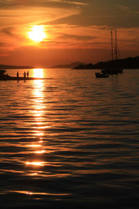 Silhouette people on sea against orange sky during sunset