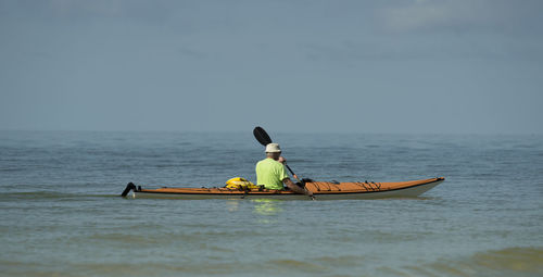 Man kayaking in sea against sky