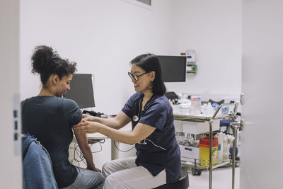 Smiling female doctor examining patient while discussing in medical clinic