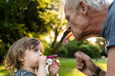 Grandfather and grandson playing with party horn blowers in park