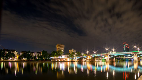 Illuminated city by river against sky at night