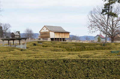 Barn on field by houses against sky