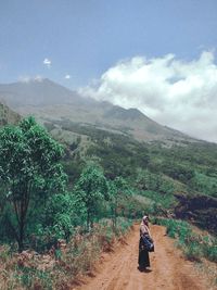 Woman standing on dirt road against mountains