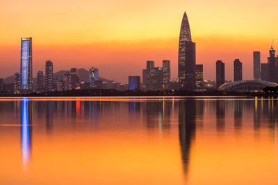 Reflection of illuminated buildings in lake against orange sky