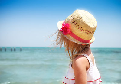 Midsection of woman with pink hat at beach against sky
