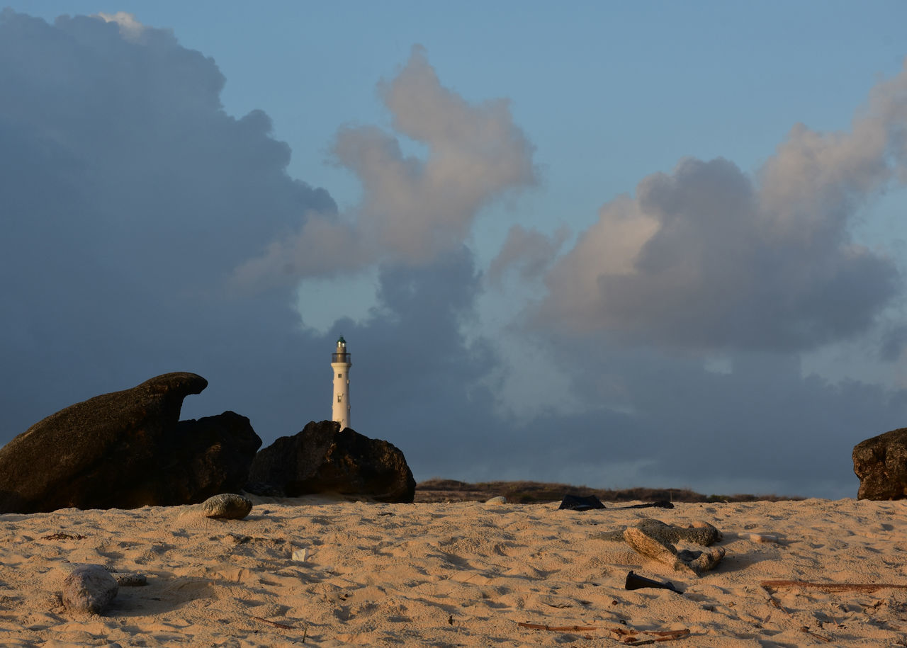 sky, lighthouse, rock, sea, cloud, nature, natural environment, land, coast, landscape, environment, architecture, sand, scenics - nature, horizon, tower, travel destinations, guidance, ocean, no people, beauty in nature, built structure, travel, outdoors, mountain, water, building exterior, beach, tranquility, day, history, rock formation, building, dawn, non-urban scene, morning