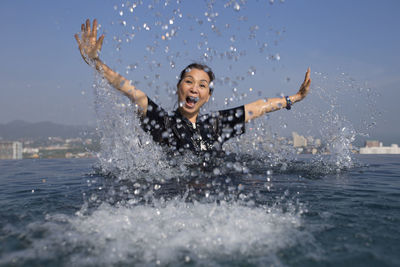 Close-up of mature woman splashing water in sea against sky
