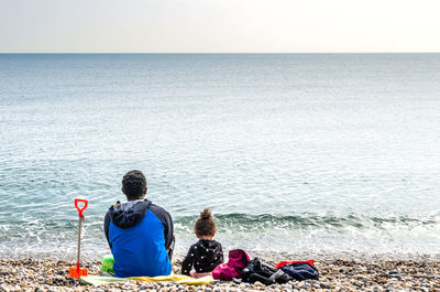 Rear view of men sitting by sea against sky
