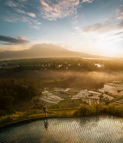 Man standing on agricultural field against sky during sunset