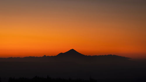 Scenic view of silhouette mountains against orange sky