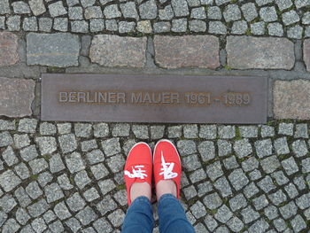 Low section of woman wearing red shoes standing on footpath by metal with text