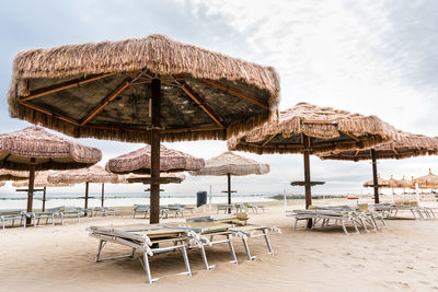 Lounge chairs and tables on beach against sky