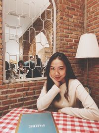 Portrait of young woman sitting on table against brick wall