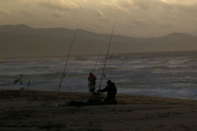 Silhouette man fishing on beach against sky during sunset