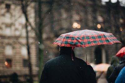 Rear view of man holding umbrella during rainy season