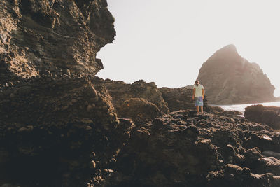 Rear view of man standing on cliff against sky