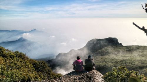 Rear view of people sitting on mountain against sky