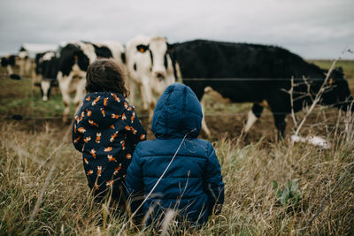 Rear view of girls looking at cows in field