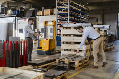 Business people inspecting metal material while standing at warehouse in factory