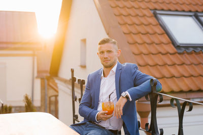 Young handsome man is sitting in an outdoor summer cafe in a blue suit and holding