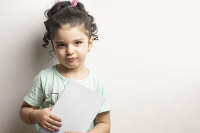 Portrait of cute girl holding paper over white background