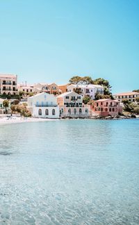 Buildings by sea against clear blue sky