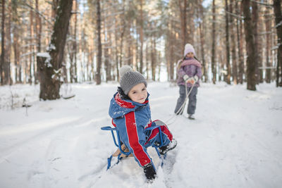 Happy friends have fun in wonderland, girl pulls sledge with sister and brother across winter forest