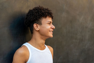 Afro latin male teenager smiling against a black wall