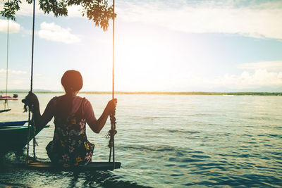 Rear view of man sitting in sea against sky