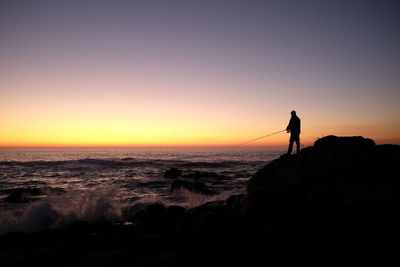 Silhouette man standing on beach against clear sky at sunset