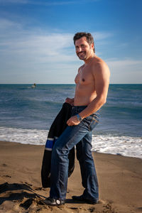 Portrait of young man standing at beach against sky