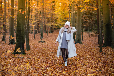 Portrait of smiling young woman standing amidst trees in forest during autumn
