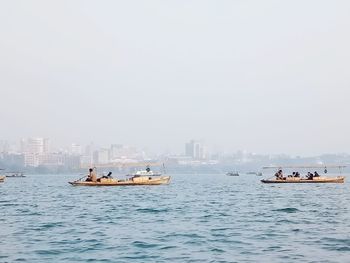 People on boats in sea against clear sky