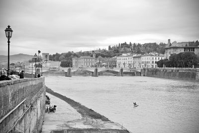 Bridge over river by buildings in city against sky